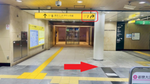 ビルの地下入り口　黄色い看板に、出口案内がかかれている　直進矢印で出口８東京ミッドタウン方面、右折矢印で出口７　赤丸で、右向きの矢印画像が表示されている