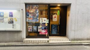 ビルの入り口　ガラス張りのドアで、内側から、名探偵コナン、おしりたんていなどのポスターが貼ってある
