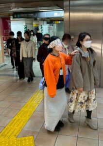 さんげんぢゃや駅で、劇団員が視覚障害しゃやくと誘導がかりやくにわかれ、ふたりひとくみで誘導れんしゅうをしています　さんくみうつっています