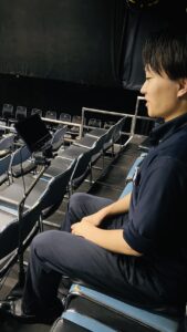 若い男性が、客席に座り字幕タブレットをながめています