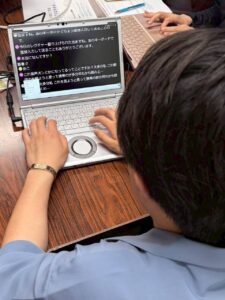 だんせいげきだんいんがパソコン画面を見ているところを後ろから撮影しています　ぱそこんがめんにはもじおこしされた会話がひょうじされています