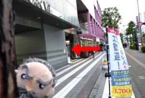 りょうごくのけいようどうろぞいのほどうの写真です てまえにびるのそくめんがうつっています 手前からふたつめのかどを赤いひだりむきのやじるしがしめしています